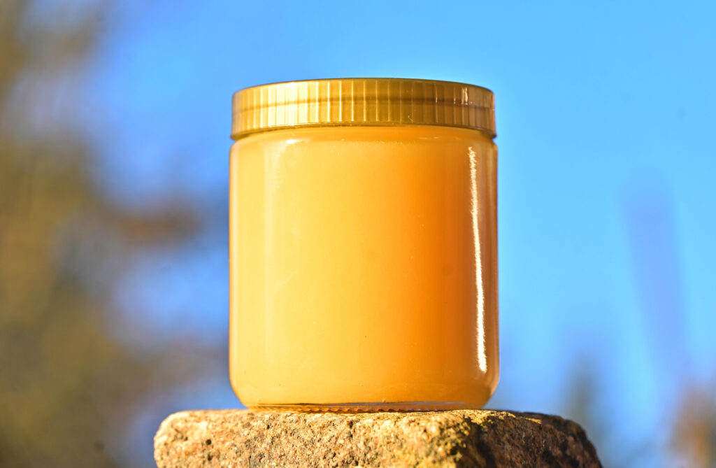 Glas mit cremigem Sommerhonig in warmem Gelbton vor blauem Himmel